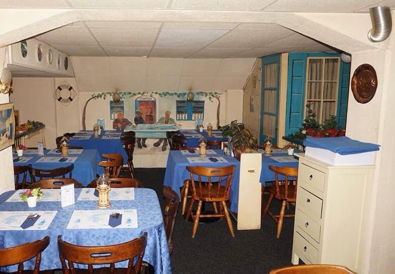 Achterzaal met muurschildering en blauwe tafelkleden
